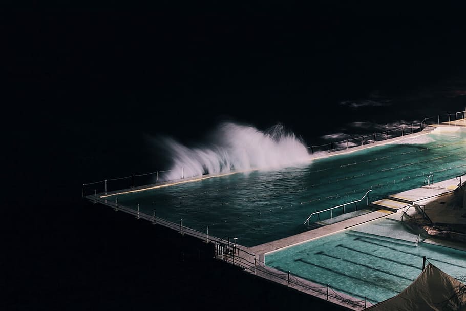 rectangular blue swimming pool during night time, sea wave banging on seawall with Olympic size swimming pool HD wallpaper