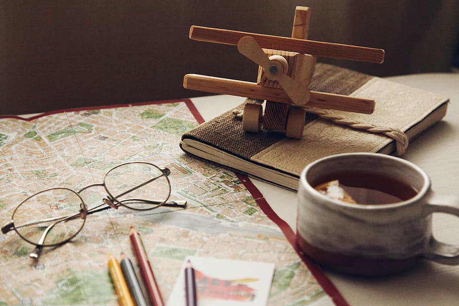 brown wooden biplane miniature on brown book, brown propeller plane miniature near white ceramic mug and black eyeglasses HD wallpaper