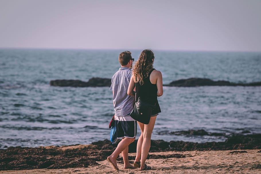 man and woman walking by the beach during daytime, man and woman walking at the shore during daytime HD wallpaper