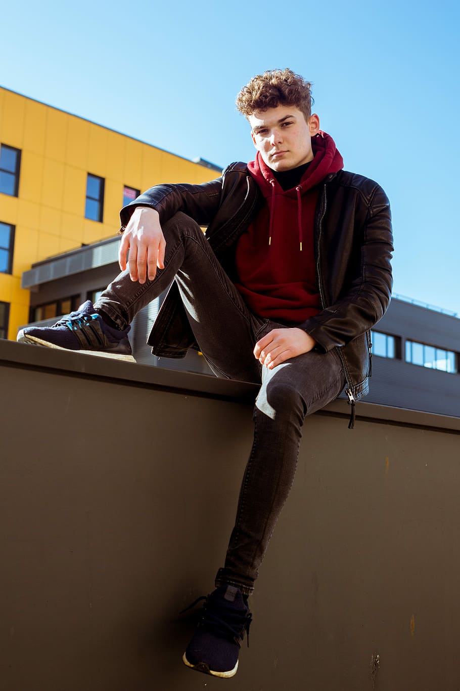 man wearing black and red jacket sitting on gray rail, building HD wallpaper