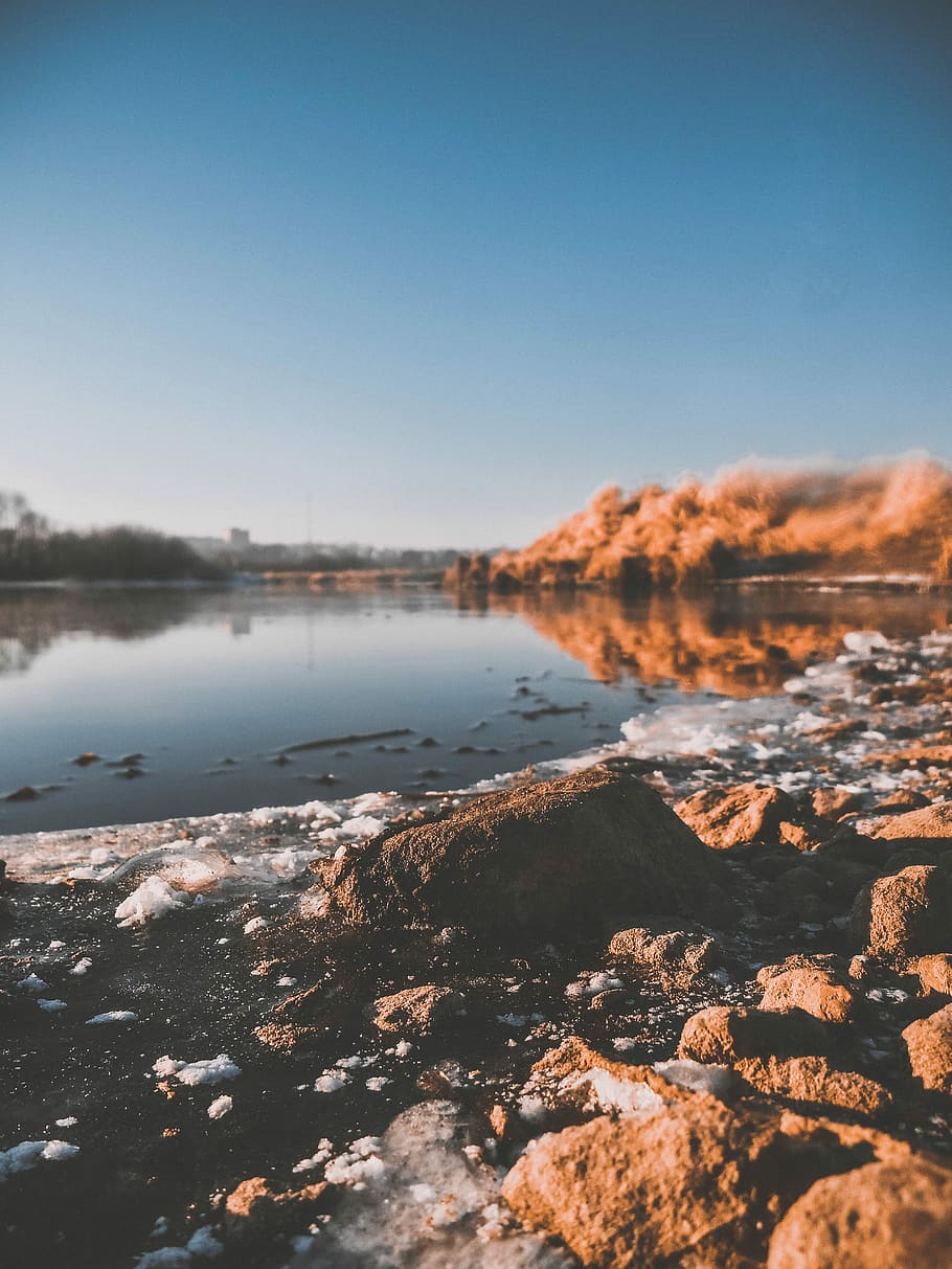 body of water under blue sky during daytime, calm body of water and rocks HD wallpaper