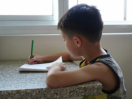 boy wearing white, black, and yellow tank top writing on paper using green pen at daytime HD wallpaper