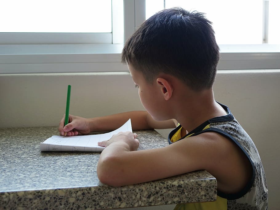 boy wearing white, black, and yellow tank top writing on paper using green pen at daytime HD wallpaper