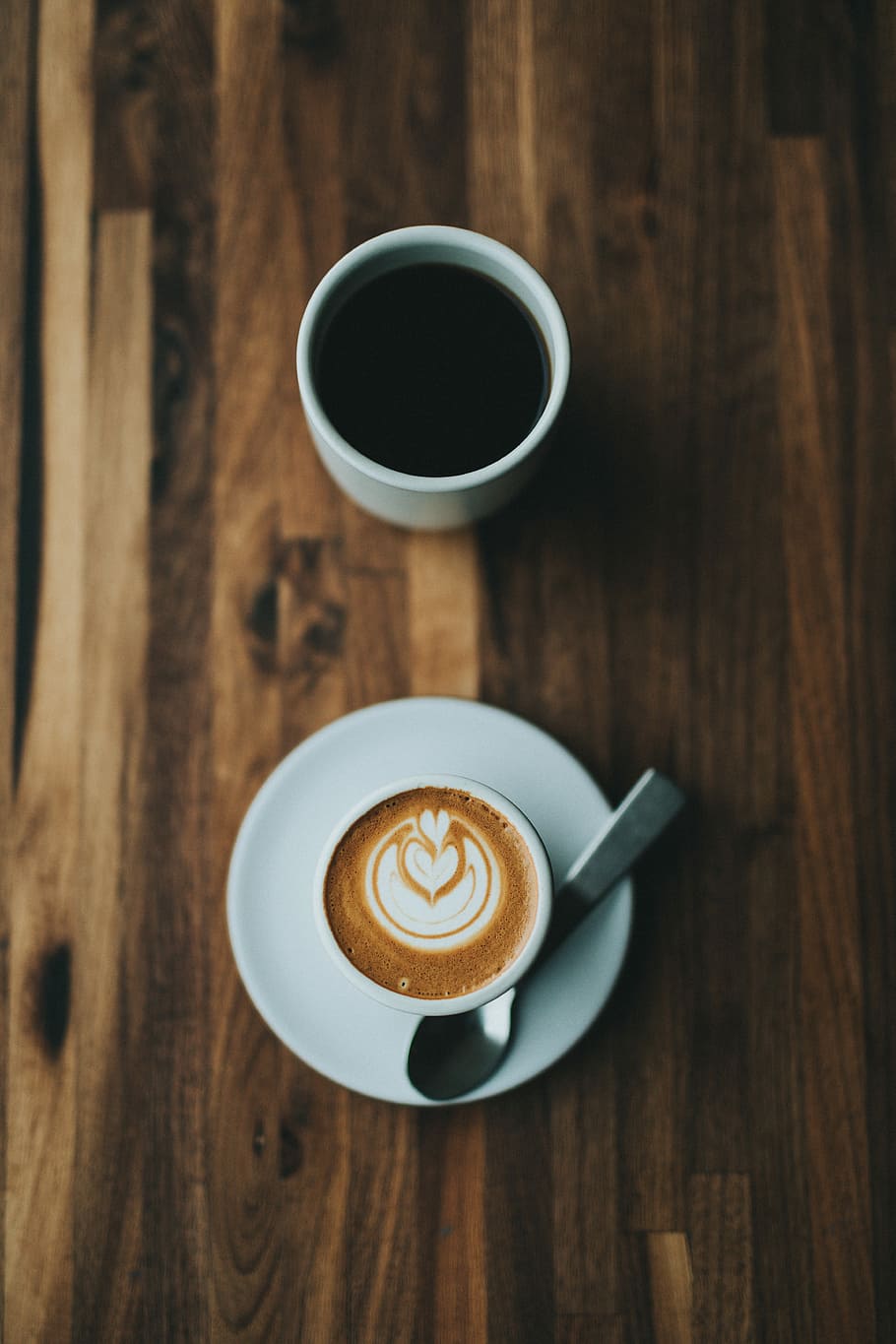 black ceramic mug filled with black liquid, top view photography of white ceramic mug with creamy latte coffee near brewed coffee on brown wooden table HD wallpaper