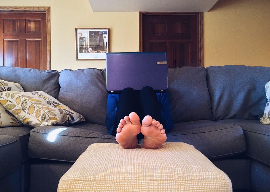 person wearing black pants sitting on gray sofa with purple laptop on lap HD wallpaper