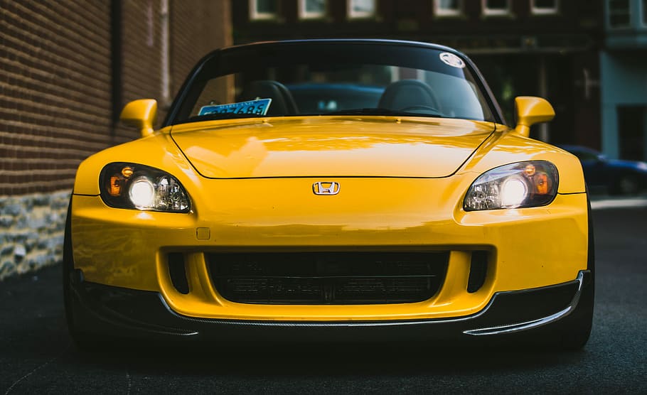 yellow Honda vehicle close-up photography, yellow Honda S2000 parked near brown concrete wall building