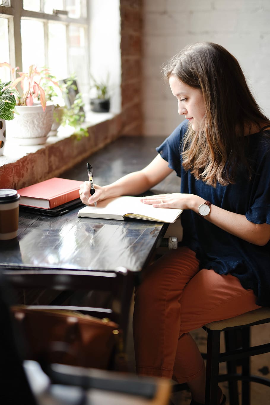 woman sitting in front of black table writing on white book near window, woman sitting and writing on book near the window HD wallpaper