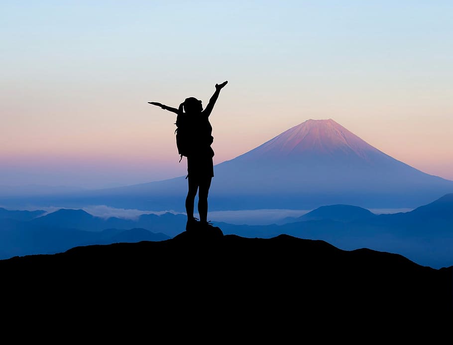 silhouette of woman raising her hands on top of mountain during daytime