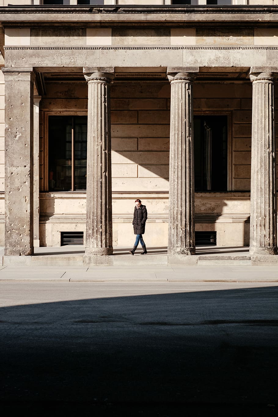 man in black jacket walks on building posts, man in black long coat standing in front of building HD wallpaper