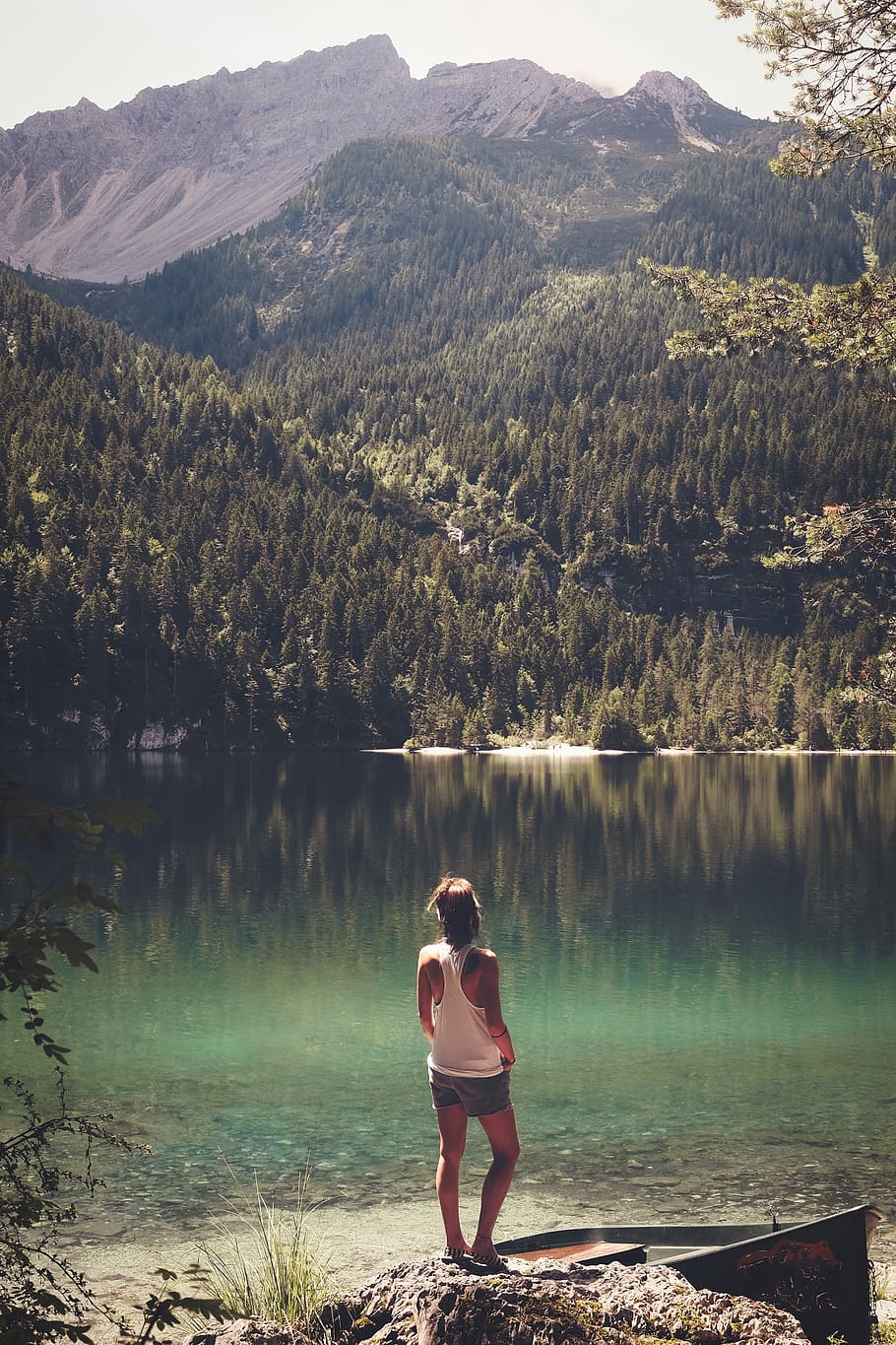 woman standing in front of body of water, woman standing on a rock looking at body of water and a mountain HD wallpaper