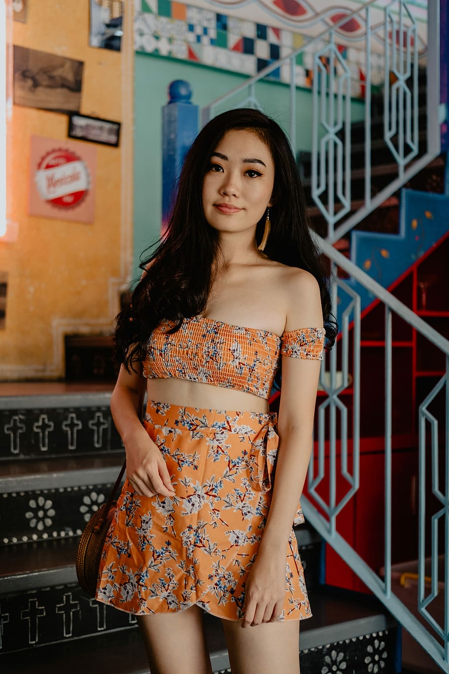 woman wearing orange crop top and skirt on the stairs, selective focus photography of woman wearing off-shoulder bustier top and rompers outfit standing at staircase