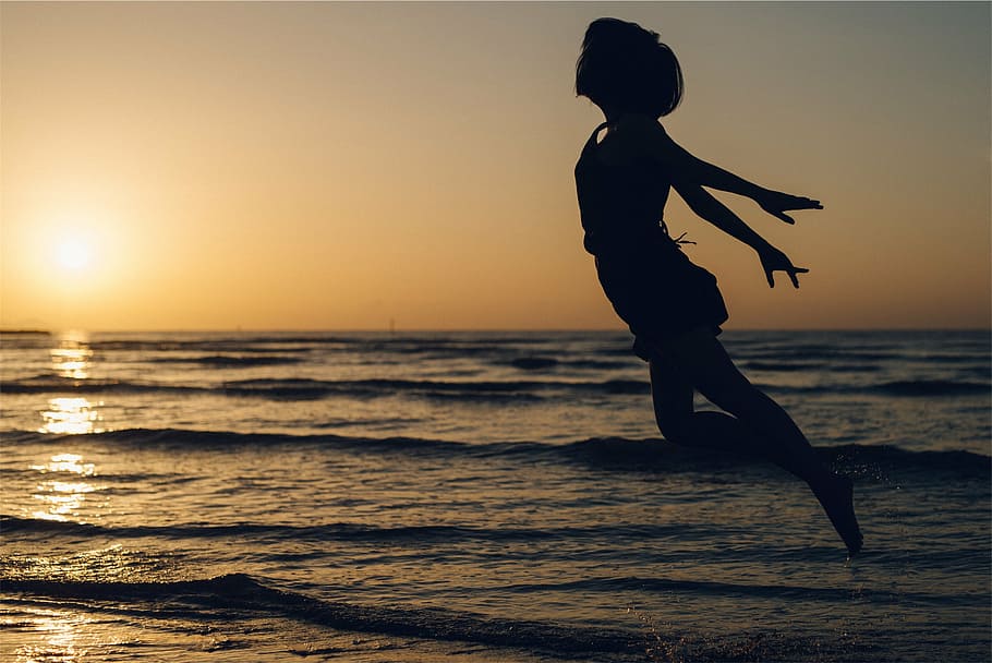 woman jumping in mid air in seashore, silhouette, daytime, sunset HD wallpaper