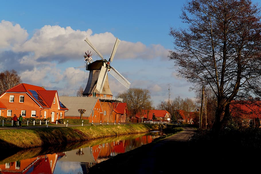 windmill on top of red house near river under blue sky and white clouds HD wallpaper