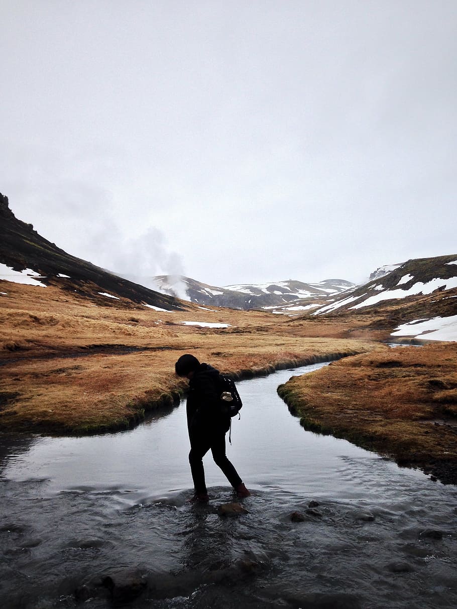 person walking on river near brown mountain range during daytime