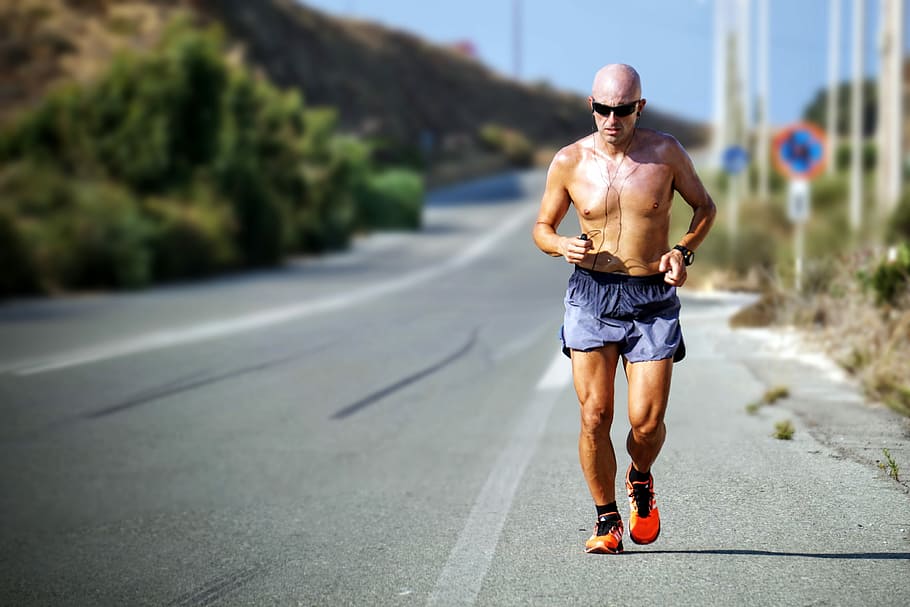 man jogging while listening using black earphones during day time, person running on roadway during day time HD wallpaper