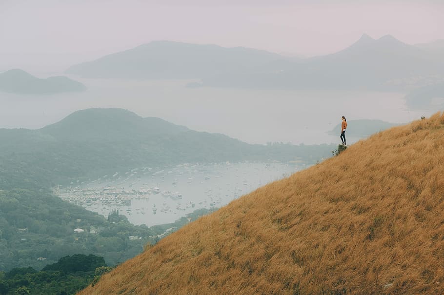 woman standing on top of stone facing village near body of water and mountain at distance, woman standing on mountain range near lake HD wallpaper
