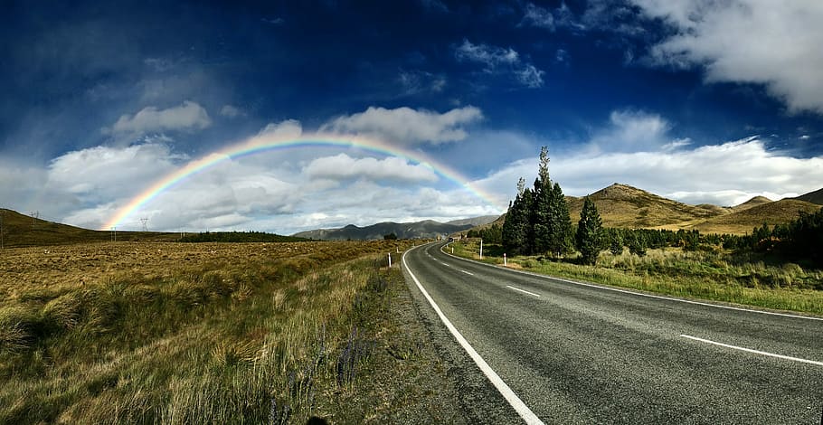 highway near trees and rainbow under blue sky, rainbow near road during daytime HD wallpaper