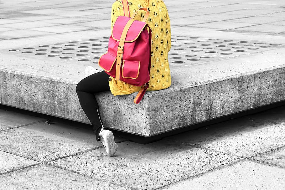 person sitting on gray surface wearing red backpack, selective