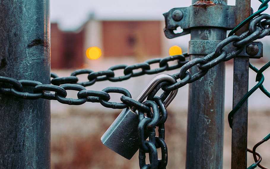 macro shot of stainless steel padlock, selective focus photography of mesh fence tied with chains and padlock
