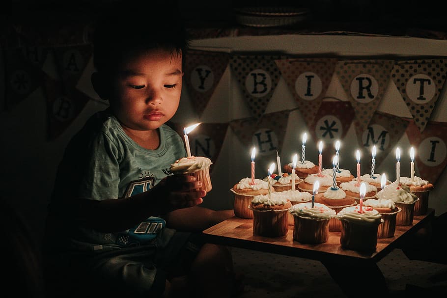 boy holding one of many cupcakes with lit candles, boy holding cupcake with lightning candle beside happy birthday buntings, HD wallpaper