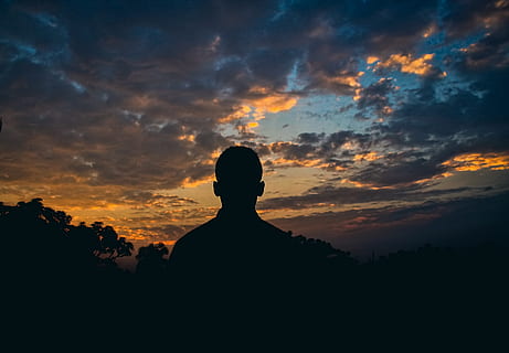 silhouette of man standing under white clouds at golden hour HD wallpaper