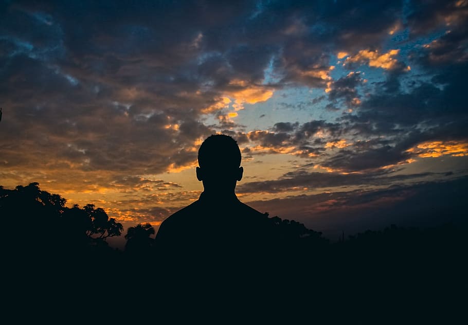silhouette of man standing under white clouds at golden hour HD wallpaper