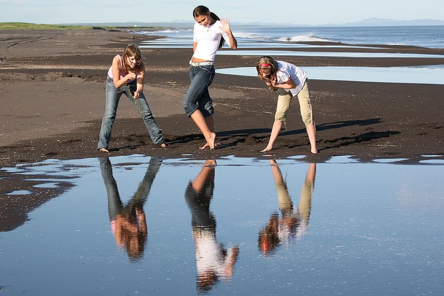 three women watching their reflection on calm body of water during daytime HD wallpaper