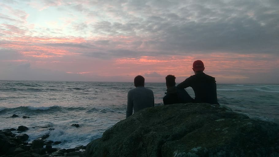 Before us is the wide sweep of the ocean, silhouette of people sitting on rock near shore HD wallpaper
