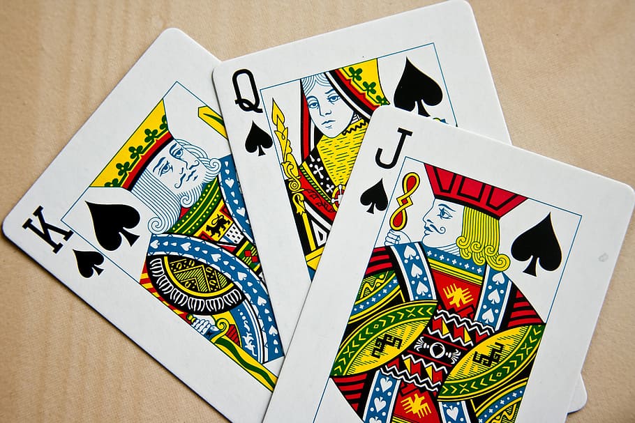 three King, Queen, and Jack of Spade playing cards on beige surface