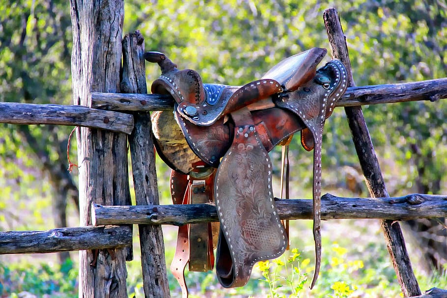 brown leather horse saddle on wooden fence during daytime, weathered saddle