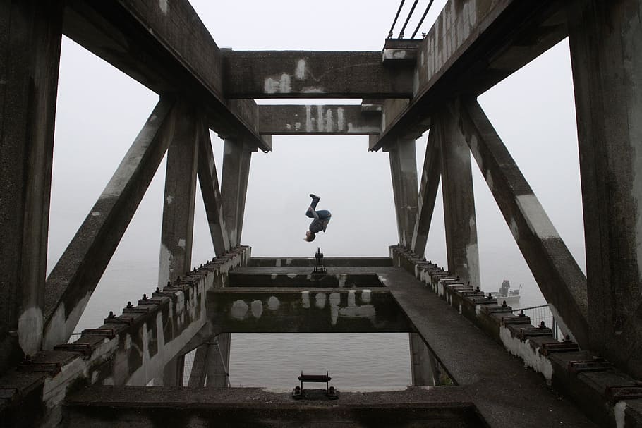 person doing back flip on building edge during daytime, man backflips on gray concrete frame HD wallpaper