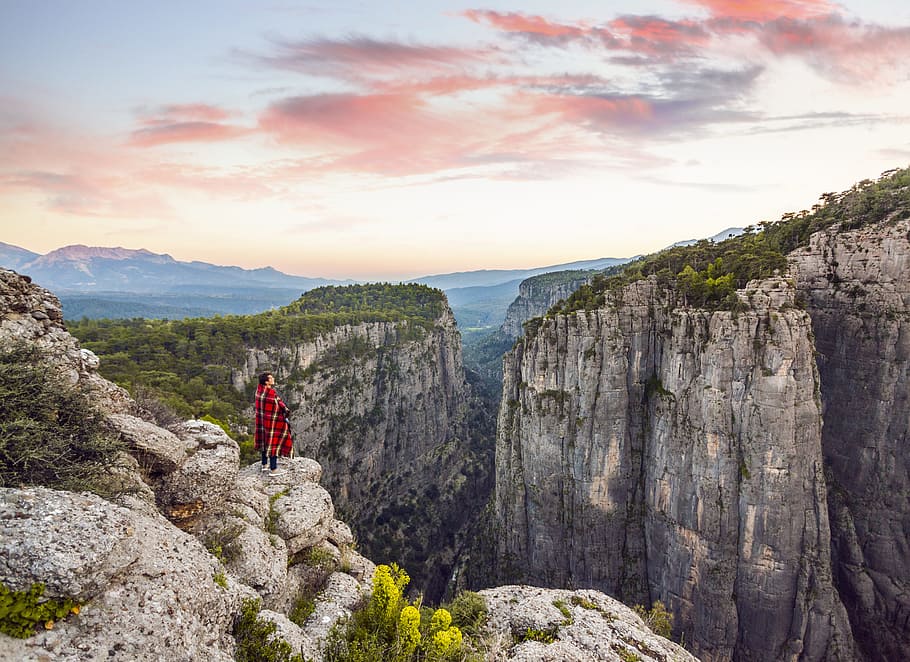 person in red shirt beside edge, person standing in front of cliff during daytime HD wallpaper