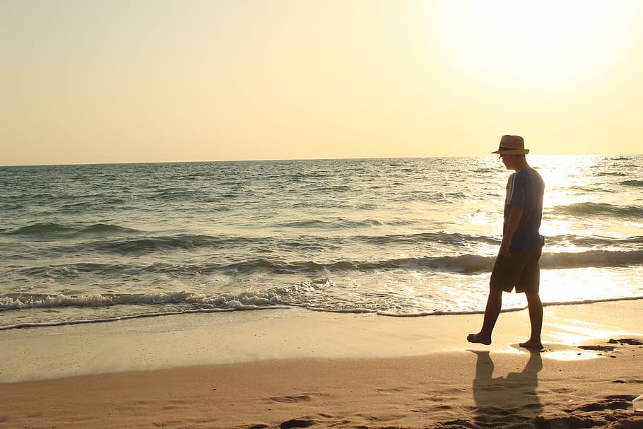 silhouette photography of person in blue shirt and beige fedora cap standing on seashore during golden hour HD wallpaper