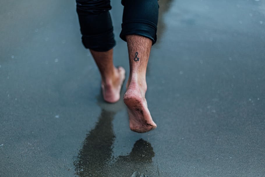 person with tattoo on foot walking on wet sands, person standing on black surface
