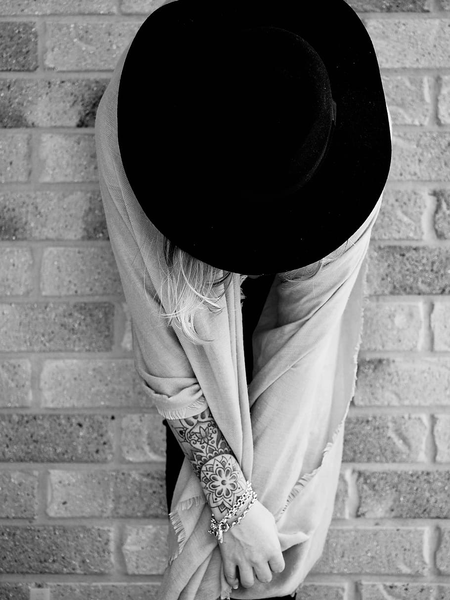 grayscale photo of woman sitting on surface, woman in scarf and black cap against brick wall HD wallpaper