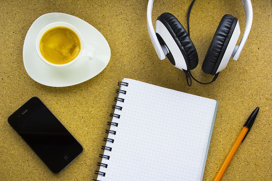 notebook between black iPhone 4 and orange pencil beside white corded headphones and white ceramic cup HD wallpaper