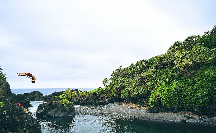 person back diving beside mountain cliff during daytime, man jumping on body of water during daytime HD wallpaper