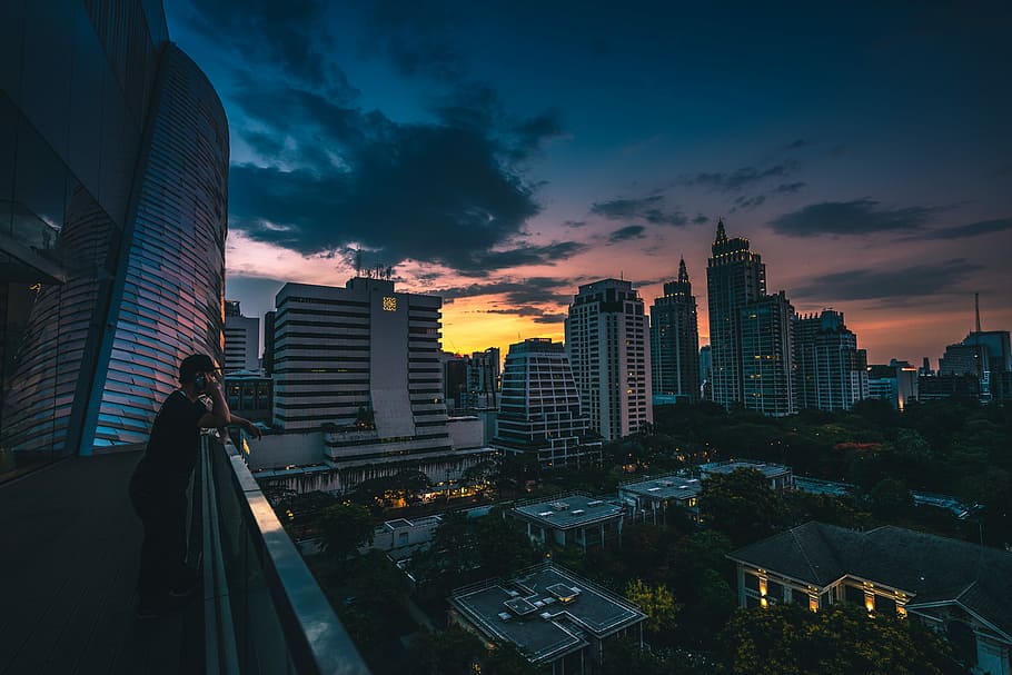 man standing near gray handrails during night time, person leaning on gray hand rail while staring the city building, HD wallpaper