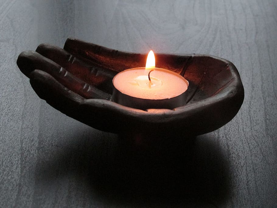 black wood carve hand candle holder with white candle on top of brown surface