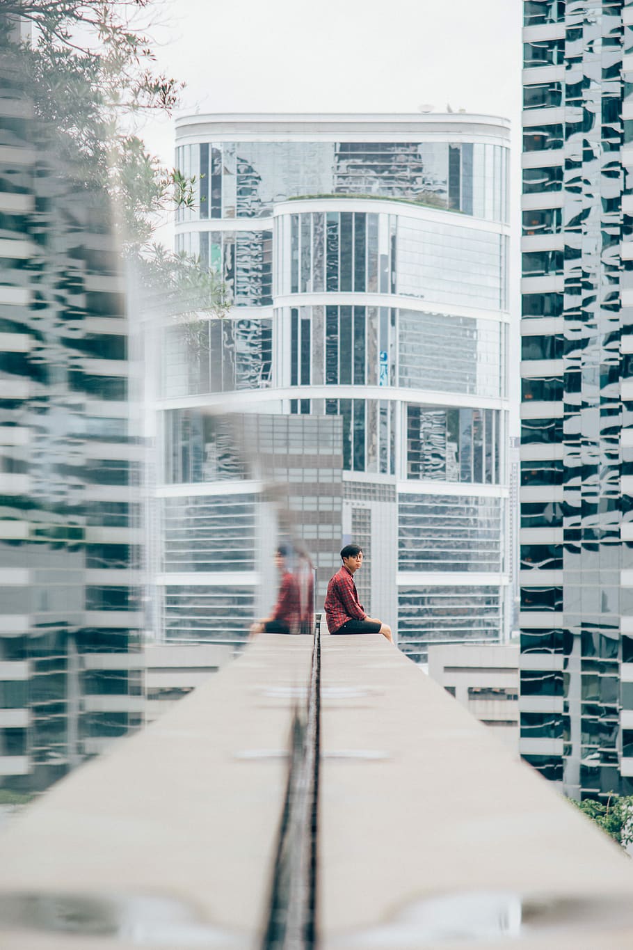 person sitting on white concrete framed near glass high rise building, man sitting on white building edge at daytime HD wallpaper