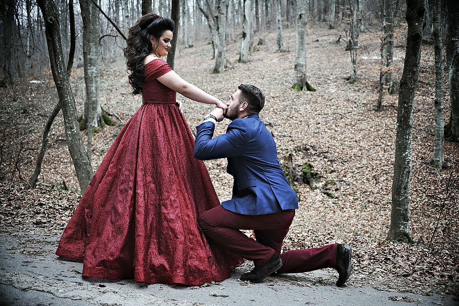 man wears blue suit and women's red dress in the forest, proposing