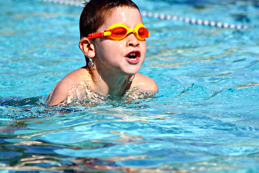 boy wearing orange and yellow diving goggles while swimming on body of water during daylight