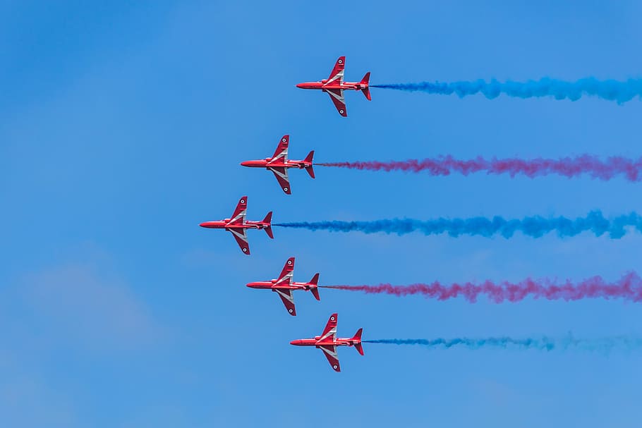 five red planes in sky, five red jets leaving blue and red contrails on blue sky