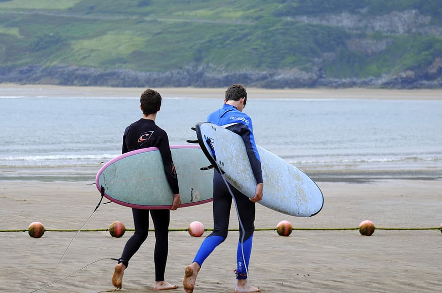 two men walking on the seashore carrying surfboards, two men walking near shoreline carrying surfboards HD wallpaper
