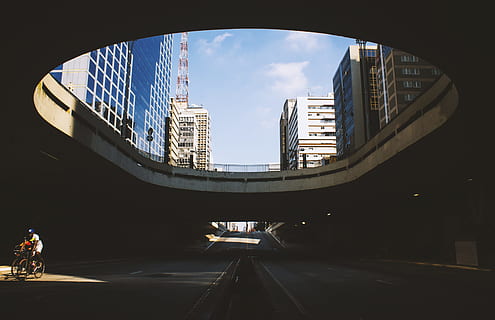 gray concrete building under blue sky during daytime, person biking on street during daytime HD wallpaper