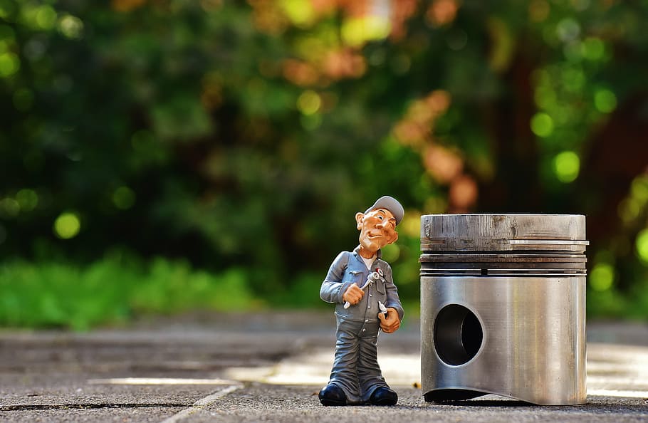shallow focus photography of man holding wrench plastic figure beside silver container during daytime