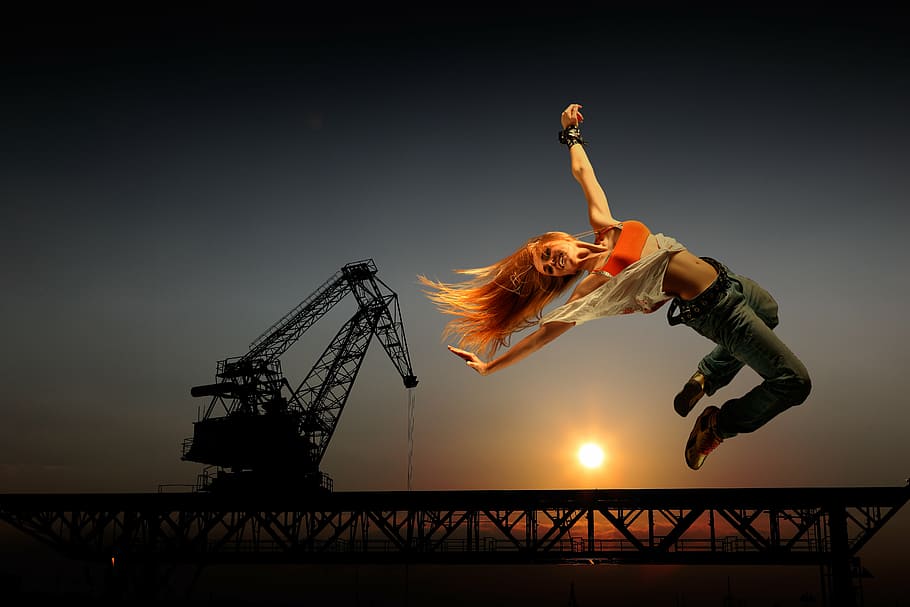 woman on air with crane background, joyful leap, jeans, acrobatics