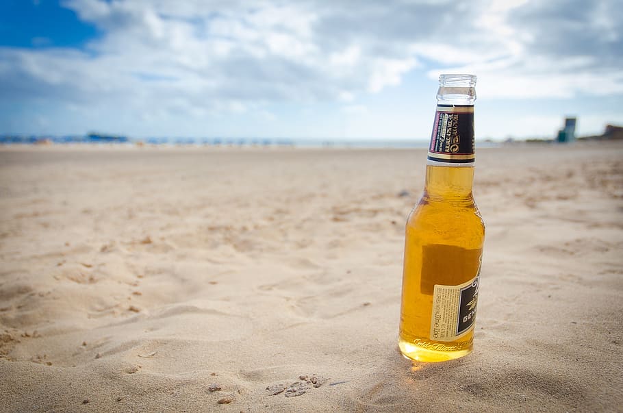 clear glass beer bottle on sand under cloudy sky, beach, vacation