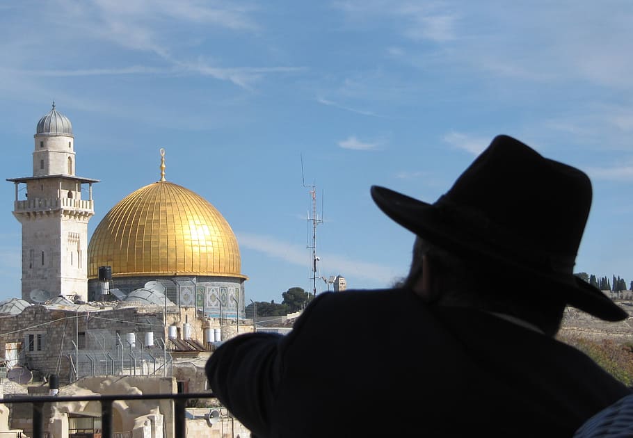 man wearing black hat near temple during day, dome of the rock