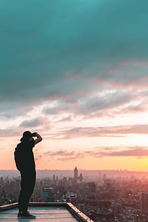 man standing on concrete building, man standing on rooftop looking in city buildings during golden hour HD wallpaper